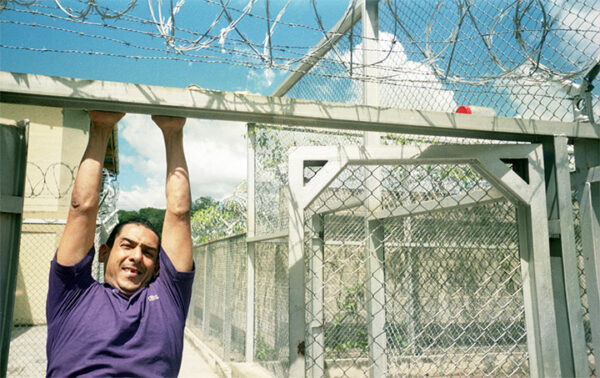 A man hangs on a gate in a prison.