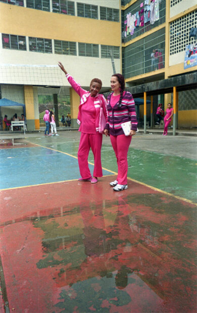 Two women stand in the foreground of a womens prison after a rain.