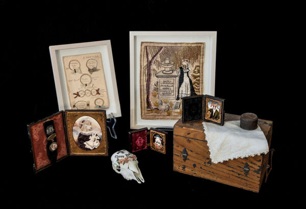 A box with handkerchief, framed family photos, a painted animal skull, and other mementos mori. 