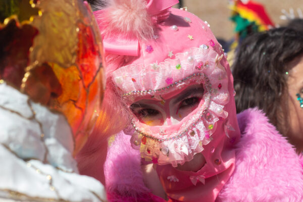 A close-up photograph of a heavily costumed reveler in New Orleans, surrounded by many people