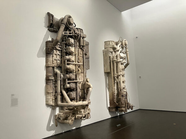 Two cast halves a large boat engine hang on a gallery wall.