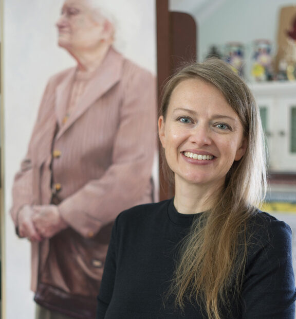 A photograph of artist Amy Werntz with a painting in the background.