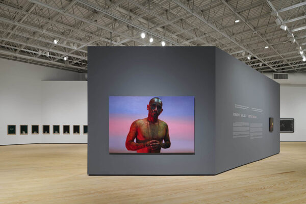 A large gallery with a painting of a tattooed man and a row of smaller paintings hanging on its walls.