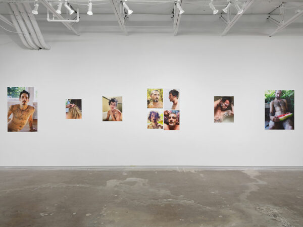 A gallery displays large color prints of photographs of young, shirtless, tattooed men.