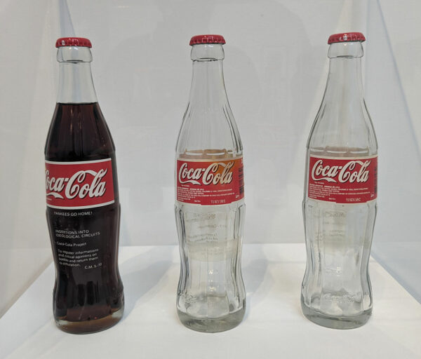 Three Coca-Cola bottles with Letra-set letters adhered to the bottles.