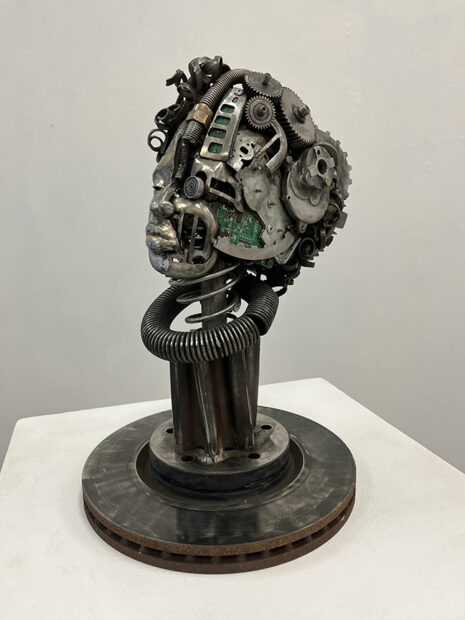 A head made from welded scrap metal including gears, a brake pad, and springs.