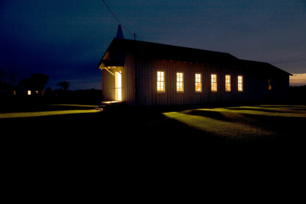 A long single story church is photographed at night with all of its lights on.