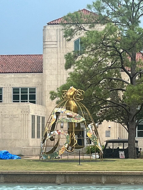 A large figurative sculpture installed outdoors witha missing head and a blue tarp nearby.