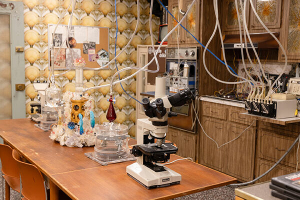 A kitchen with 70s era design houses an improv laboratory with mocroscopes and obsolete science equipment on its countertops.