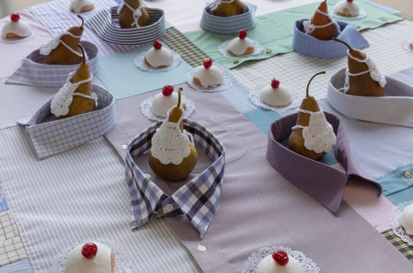 A table top covered with button down shirts has pears with doilies sitting atop it.