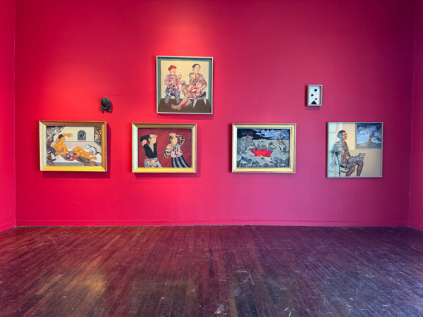 A gallery with red walls displays several surrealist paintings hung salon style.