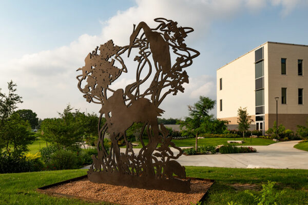 A large steel sculpture of bird silhouettes in foliage installed outside.