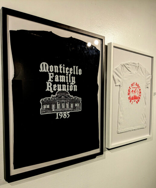 Two framed t-shirts hang on a gallery wall.