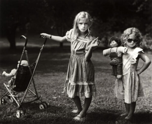 A black and white photograph of two young girls with baby dolls.