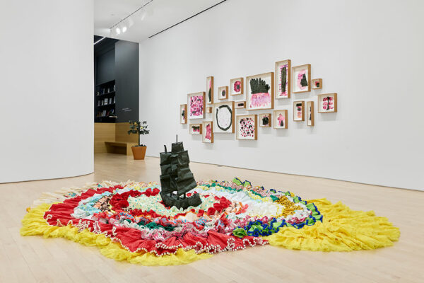 A small soft sculpture of a Spanish ship sitting atop flamenco dresses on the gallery floor.