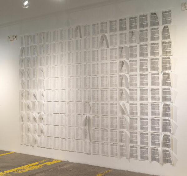 A grid of letter-sized sheets of paper cover a gallery wall floor to ceiling.