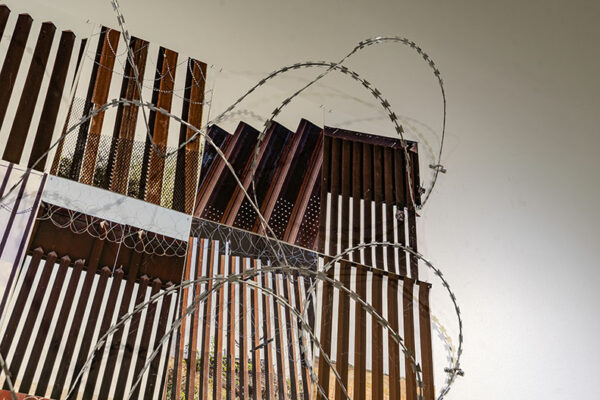 A collection of photographs of different sections of the border wall installed with razor wire in a gallery.