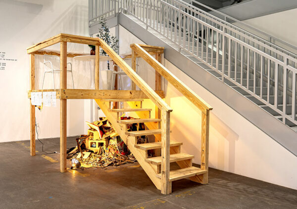 Near a stairwell a wooden platform hosts a table with flowers and menus above a pile of rubble.