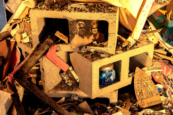 Debris piled up underneath a platform in an art gallery features cinderblocks, photographs, damaged paintings