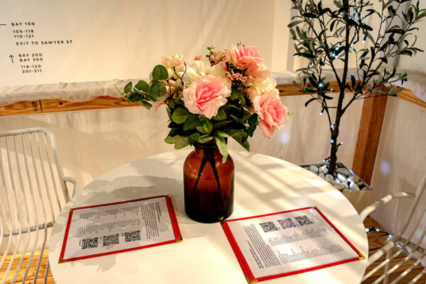 A table top with menus a vase of flowers and a large plant in the background.