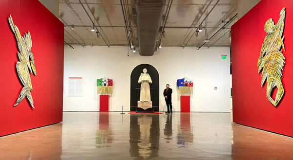 A man stands before a sculpture of Saint Anthony in a gallery with sculptures and paintings.