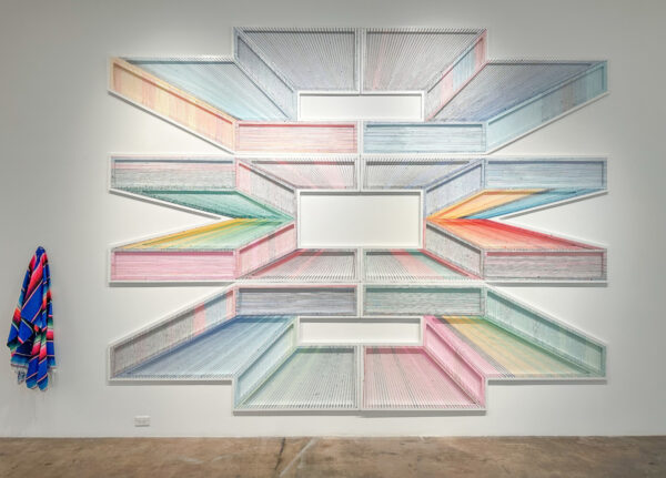 An installation image of a large installation by Adrian Esparza featuring a serape and an abstract thread work.