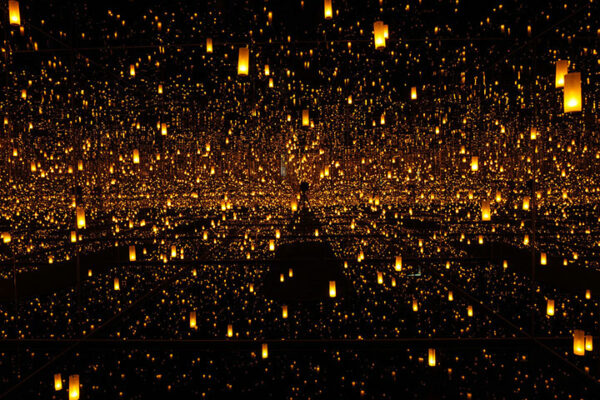 A field of candles reflect in the darkness against a wall of mirrors.