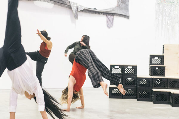 Four movement artists perform amidst sculptures in a gallery.