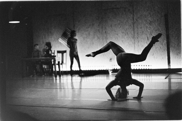 A black and white image of movement artists performing on a low-lit stage.