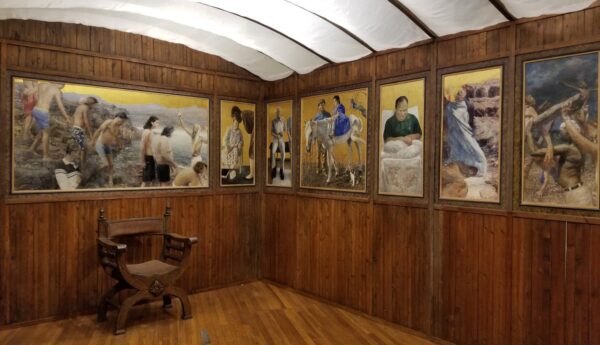 An installation photograph of a built environment that resembles the interior of chapel with paintings hanging on the walls.