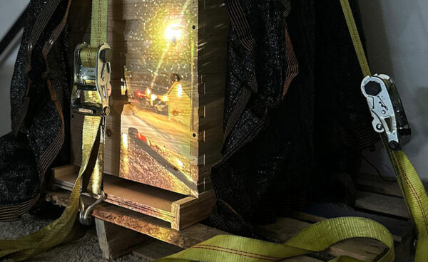 A darkened room with a video projecting atop a stack of wooden bee hives.