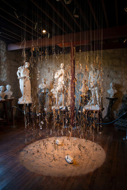 Strings hang from the ceiling of a museum with items attached to them.