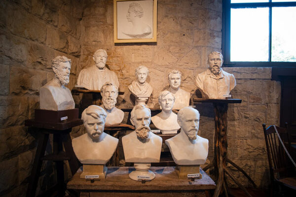 Ten white busts arranged on tables in a low-lit room.