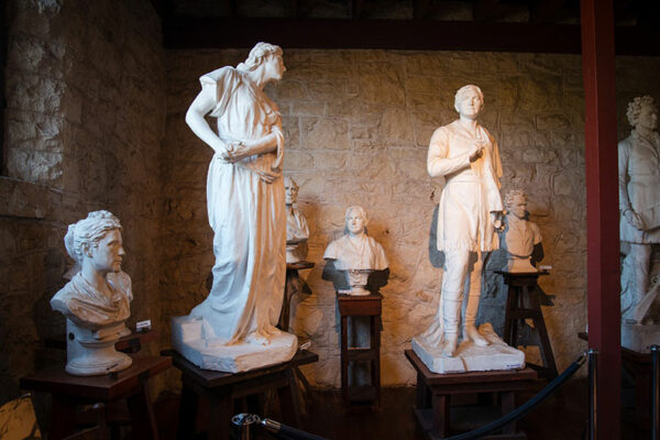 Two full-figure sculptures and four busts in a low-lit room.