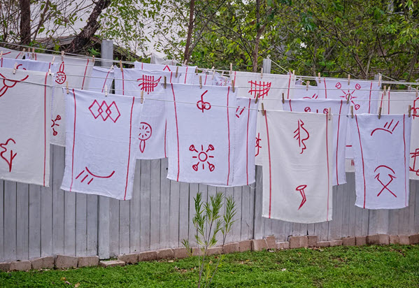 A photograph of fabric works featuring red symbols on white fabric, hanging on a clothesline. 