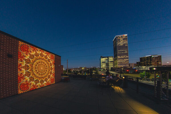 A nighttime photograph of a rooftop with a projected video on a brick wall.