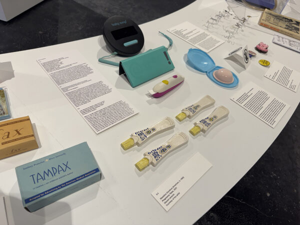 A table featuring artwork alongside period and reproductive care products from the exhibition "Designing Motherhood."