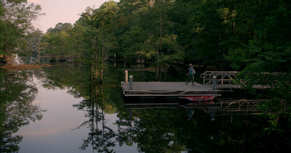 A woman walks out on a dock on a river.