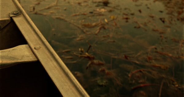 The water of a river is seen from over the edge of an aluminum canoe.