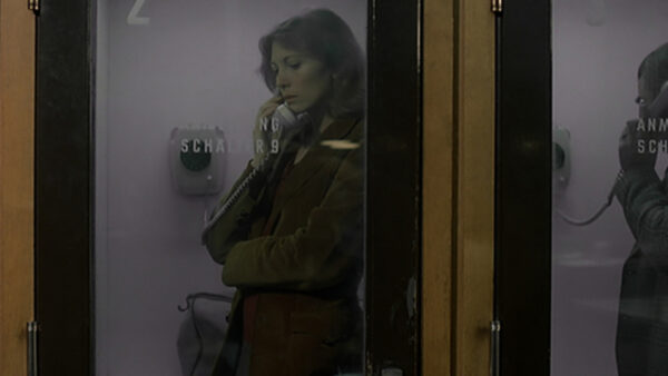 A woman stands inside a public phone booth making a call.