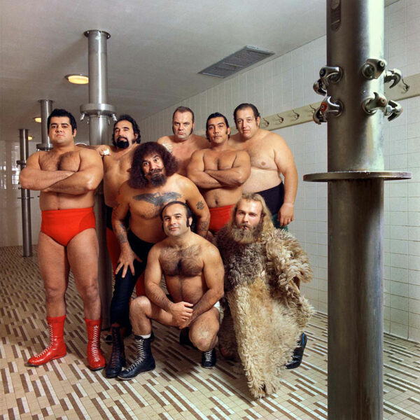 * muscular men pose together staring directly into the camera and wearing wrestling shorts and boots one man is wrapped in fur.