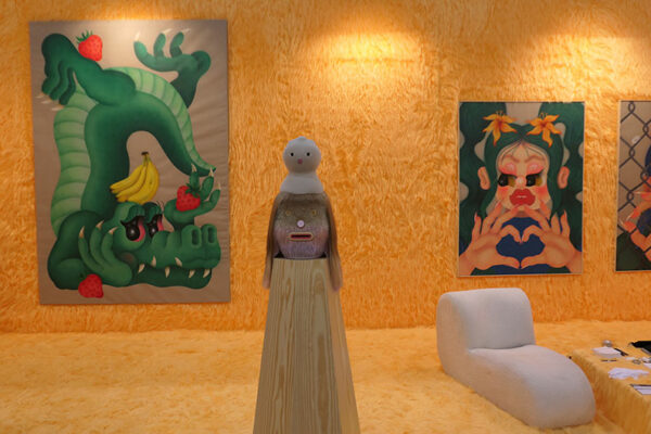 A gallery with yellow walls and fuzzy shag rug has two paintings hanging on its walls.