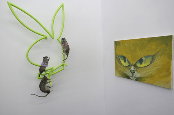 Three taxidermied mice are positioned on a a green Playboy bunny sculpture next to a painting of a cat.