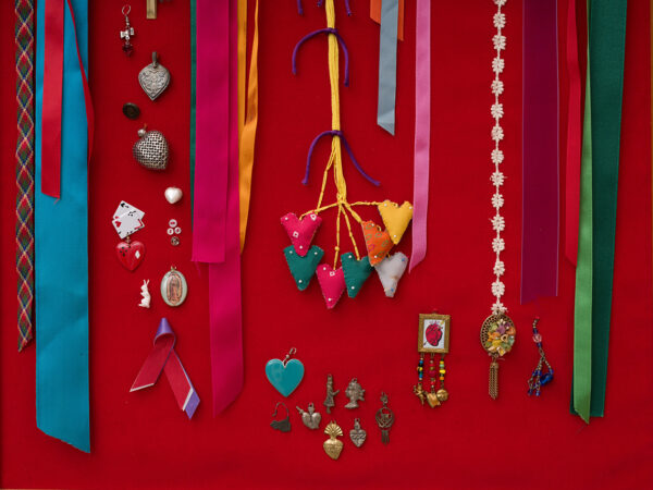 A photograph of an installation image featuring small jewelry charms and ribbons pinned to a fabric