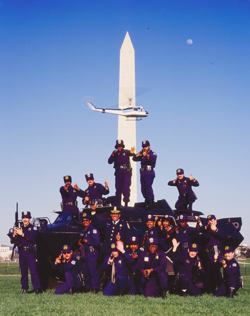 A group of SWAT officers pose with guns aimed at the camera atop an armored vehicle on the National Mall.