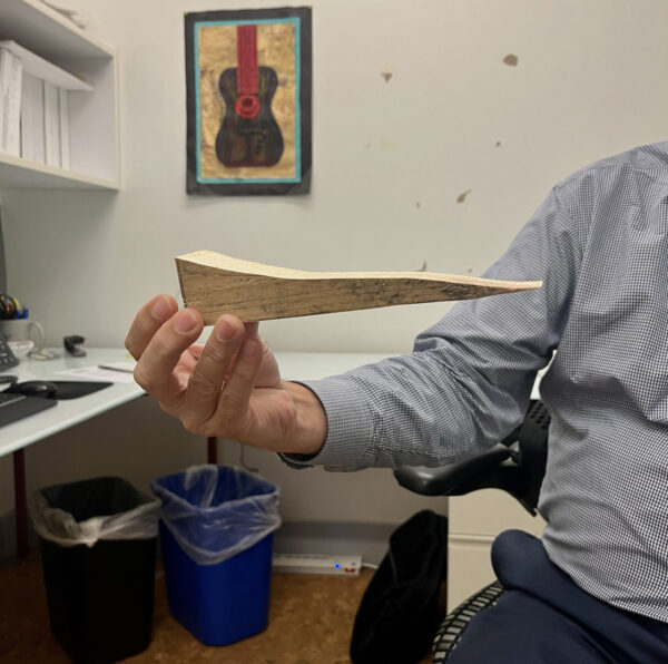 A photograph of a person sitting in a chair holding a small wooden sculpture.