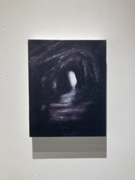 A small black painting with a white light emanating at the center