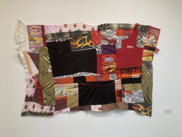 An assortment of chip bags and fabric scraps in red and black are sewn together in a flat fabric panel that is not uniformly square