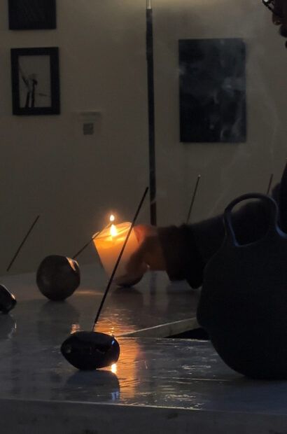 A man holds a lit candle on a table with multiple incense sticks.