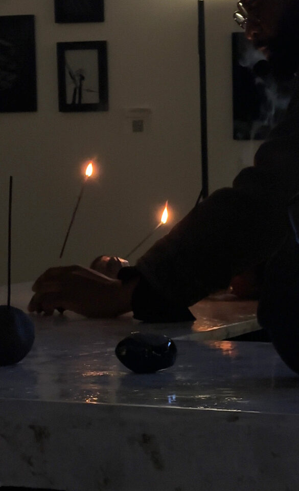 A man places two lit incense sticks in holders in a dimly lit room.